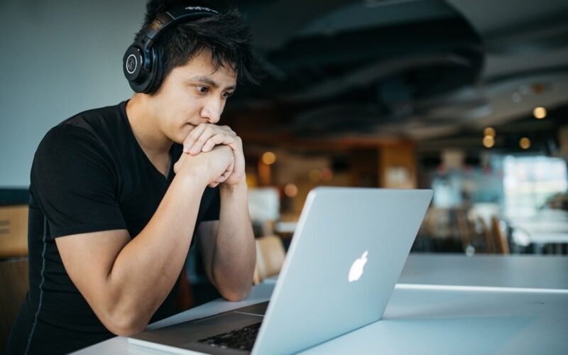 Eftertänksam person med hörlurar framför en laptop på ett kafé